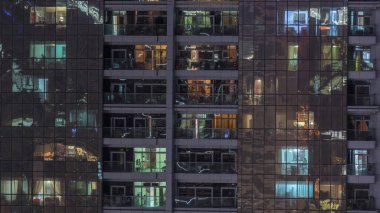 Night view of exterior apartment building timelapse. High rise skyscraper with blinking lights in windows with people moving inside clipart