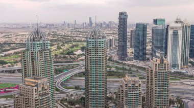 Dubai Marina gökdelenleri ve Jumeirah göl kuleleri Birleşik Arap Emirlikleri 'nde hava gününden geceye geçiş zamanlarını gösteriyor. Kavşağı olan bir yolda trafik