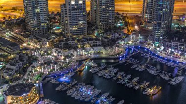 Dubai Marina Limanı 'nda gece vakti deniz kenarında modern yatlar var. Kanalda yüzen tekneler kuleleri ve gökdelenleri çevreledi..