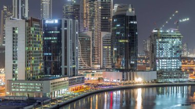 Gece şehrin merkezinde parlak gökdelenler ve inşaatlar. İş Körfezi, Dubai, Birleşik Arap Emirlikleri hava zaman çizelgesi yakınlarındaki kanalda ışıklandırılmış yol.