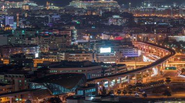 Gece şehir silueti, yolların ışıkları ve limanda büyük çekici gemilerle Dubai Creek, Dubai, Birleşik Arap Emirlikleri yakınlarındaki metro hattında.