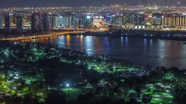 Dubai Creek, Deira 'da, Dubai, Birleşik Arap Emirlikleri' nin arka planında, yeşil ışıklı park ve yolun yanındaki gece şehri.
