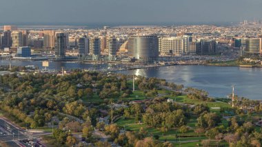 Güneş batarken Dubai Deresi ve Deira 'da arka planda deniz bulunan Park ve Mavi Nehir yakınlarındaki yeni modern binaların akşam manzarası Birleşik Arap Emirlikleri
