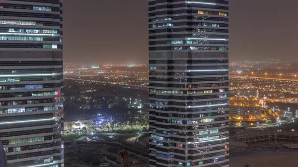 Office buildings in Jumeirah lake towers district night timelapse with blinking lights in windows in Dubai. Aerial view from above with modern skyscrapers