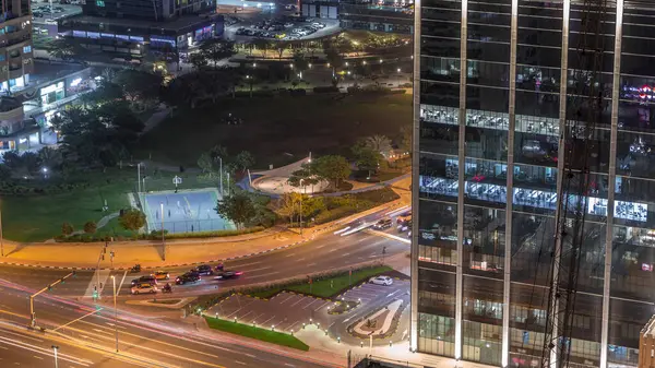 Residential and office buildings in Jumeirah lake towers district night timelapse with park and traffic on intersection in Dubai. Aerial panoramic view from above with modern skyscrapers