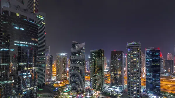 Residential and office buildings in Jumeirah lake towers district during all night timelapse with lights switching off in Dubai. Aerial panoramic view from above with modern skyscrapers