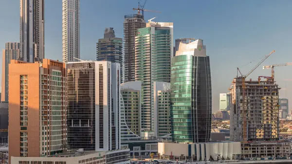 Futuristic skyscrapers near canal aerial timelapse with blue sky and restaurants in coast at sunny day on Business Bay with reflection from glass, Dubai, United Arab Emirates
