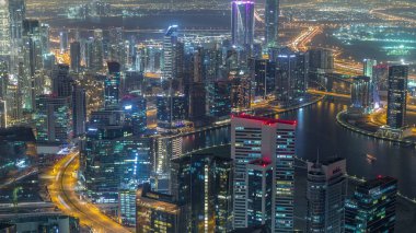 Dubai gece zaman atlamalı iş bölümü kuleleri panoramik havadan görünümü. Yapım aşamasındaki bazı ışıklı gökdelenlerin, kanalın ve yeni kulelerin çatı görünümü.