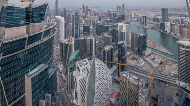 Dubai'deki iş bölümü kulelerinin panoramik havadan görünümü gece geçiş saati. Gün batımından sonra yapım aşamasında olan bazı gökdelenler, kanal ve yeni kulelerin çatı görünümü.