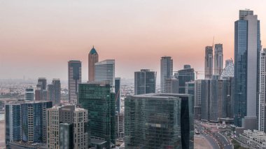 İş sahasında gece gündüz kuleler aydınlandı. Gece geçiş zamanı. Bazı gökdelenlerin çatı manzarası ve inşaat halindeki yeni kuleler. Yollarda trafik ve pencerelerde ışıklar