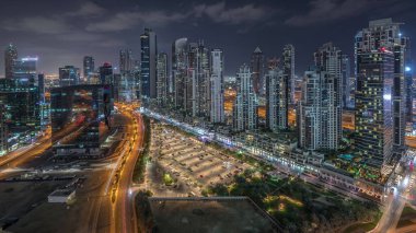 Business Bay, Dubai, Uae 'de birçok gökdelenle aydınlanmış konut ve ofis kompleksi. Körfez Bulvarı Parkı 'nın yanındaki büyük otoparkta arabalar ve trafik vardı.