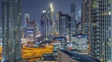 Dubai Finansal Merkezi semti, aydınlatmalı modern gökdelenler, gece zaman çizelgesi. Şehir merkezinden hava görüntüsü caddelerde ve kavşakta trafik var