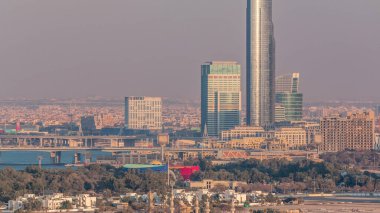 Gün batımında festival şehri ile Dubai Creek ve Garhoud Köprüsü havadan görünümü. Güneş gökdelen cam yüzeyinden yansıyan. Dubai - Bae