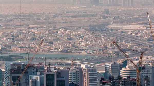 Aerial view of Business Bay area with a construction site and traffic on highway timelapse in Dubai. Houses and villas in morning haze