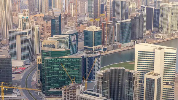 Panoramic aerial view of business bay towers in Dubai at evening timelapse. Rooftop view of some skyscrapers, canal and new towers under construction.
