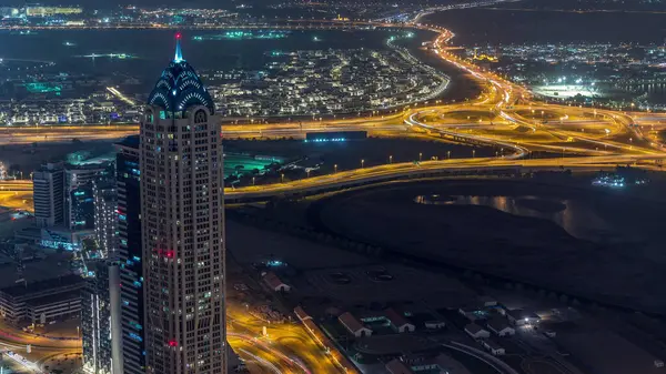 Panoramic aerial view of business bay towers in Dubai night timelapse. Rooftop view of some illuminated skyscrapers, traffic on crossroad and new towers under construction.