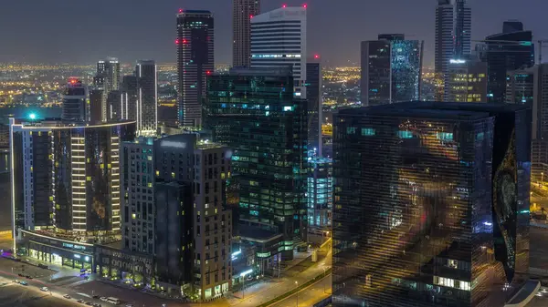 Panorama of Business bay Dubai from night to day transition timelapse. Aerial view with illuminated towers and skyscrapers. Traffic on the road with lights.