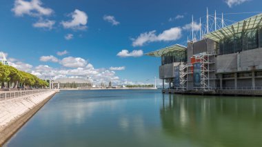 Panorama showing Lisbon Oceanarium timelapse, located in the Park of Nations or Parque das Nacoes. The largest indoor aquarium in Europe. Waterfront with green trees and clouds on a blue sky. Portugal clipart