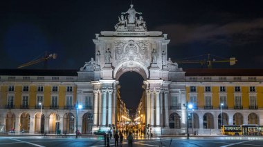 Triumphal arch at Rua Augusta and at Commerce square night timelapse in Lisbon, Portugal. Cloudy sky behind illuminated historic buildings