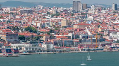 Lizbon Tarihi Merkezi 'nin panoraması Tagus veya Tejo Nehri' nin güney kıyısından izlendi. Kırmızı çatılı binalar ve su ve vinçlerde yüzen gemiler.