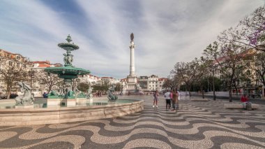 Portekiz 'in Lizbon şehrinde Baixa bölgesinin zaman aşımına uğramış sütununda çeşme ve anıt bulunan Rossio Meydanı. Mavi gökyüzünde bulutlar ve mozaik fayanslar