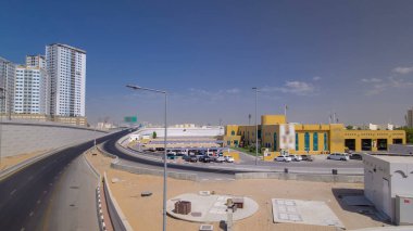 Ajman 'da üst geçitte yol trafiği, köprüden gündüz vakti havadan görüntü. Birleşik Arap Emirlikleri 'nin arka planında kuleleri olan şehir manzarası.