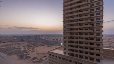 Ajman 'da çatıdan gece kuleye kule ve kavşakta trafik olan şehir manzarası. Birleşik Arap Emirlikleri 'nde gün batımından sonra aydınlanan binaların hava manzarası.