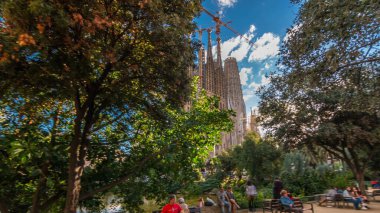 Sagrada Familia, Barselona, İspanya, timelapse hyperlapse büyük bir Roma Katolik Kilisesi. Sonbahar günü, yeşil ağaçlar, mavi bulutlu gökyüzü
