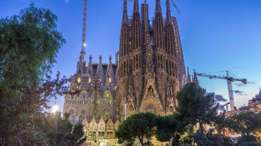 Sagrada Familia: İspanya 'nın Barcelona kentindeki Iconic Roma Katolik Kilisesi' nin Gündüzden Geceye Geçiş Süreci. Kuleler ve Turnalar Yakınlardaki Gölün Huzurlu Sularında Yansımaya Karşı Duruyor