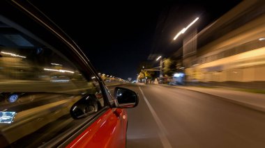 Hızlı arabanın yanından gelen bir drivelapse, gece caddesinde hızla ilerliyor. Işıklar yüksek hızda arabayı yansıtıyor. Modern bir şehrin hızlı ritmi. Bulanık hareket