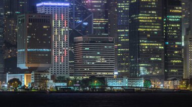 Viktorya Limanı 'ndaki kulelerin yansımalarıyla birlikte Hong Kong gece görüşü. Gökdelenlerde parlayan pencereler