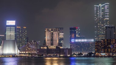 Hong Kong Kültür Merkezi. Rıhtımda. Duvarında renkli ışık yansıması var. Victoria limanının suyuna yansıyan modern yüksek kuleler.