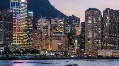 Günümüz modern gökdelenlerinde ışıldayan pencereleri olan Hong Kong 'un silueti Victoria Limanı' ndan gece geçişi. Rıhtımın manzarasını kapat. Gün batımından sonra güzel gökyüzü