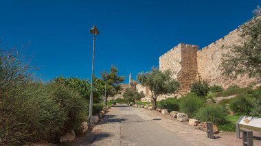 Antik kutsal Kudüs zaman tünelinin savunma duvarı. Parlak güneş tarafından aydınlatılan hiperhız. Harika yeşil çimenler ve mavi gökyüzü. Yolda trafik vardı.