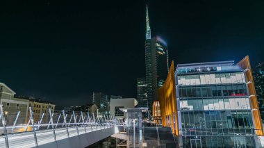 Milan Porta Nuova 'nın iş bölgesinde gece geçiş zamanı. Gökdelenlerin pencerelerinde yaya köprüsü ve ışıklar