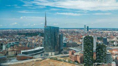 Milan 'ın modern kuleleri, gökdelenleri ve Garibaldi tren istasyonunun çatıdan iş bölgesinin zaman çizelgesi manzarası. Kırmızı çatılı evler. Yazın mavi bulutlu gökyüzü