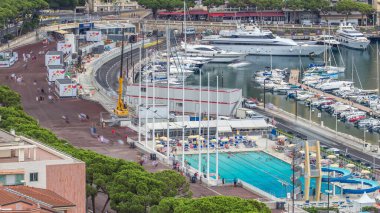 Monaco zaman diliminde deniz kenarında yüzme havuzu, insanlar şemsiyelerin altında dinleniyor ve arka planda binalar var. Havadan görünüşlü. Yolda trafik vardı.