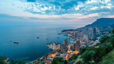 Monako 'nun havadan panoramik manzarası. Büyük Corniche yolundan geceye geçiş zamanı, Monako France. Akşam aydınlatması. Limanın suyundaki yansımalar