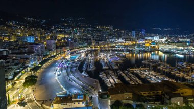 Monte Carlo 'nun Panorama' sı geceleyin Herkül Limanı ile Monako köyündeki gözlem güvertesinden hızla yükseliyor. Liman manzaralı, aydınlık binalar ve yatlar. Yolda trafik vardı.