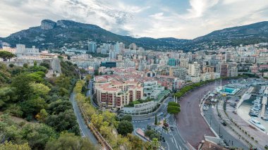 Monte Carlo 'nun Panorama' sı, Herkül Limanı yakınlarındaki Monaco köyündeki gözlem güvertesinden gece gündüz. Aydınlatılmış binalar ve arka plandaki tepeler. Yolda trafik vardı.