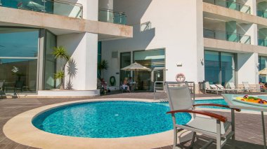 Güneşli yansımaları ve mavi suyu olan küçük bir otel yüzme havuzu ve meyveli bir masa.