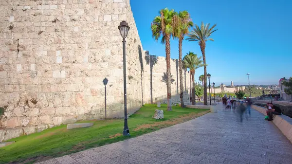 古代の聖なるエルサレムの防御壁は 明るい太陽に照らされた超過度を経ます ヤシと青空と素晴らしい緑の芝生 ストック写真