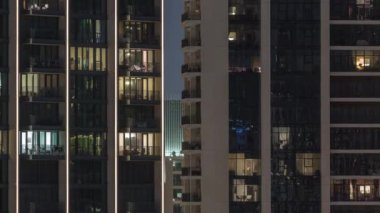 Kulelerdeki ve gökdelenlerdeki odalarda akşam ışığı. Şehrin yerleşim bölgesinde parlayan pencereleri olan uzun apartman blokları..