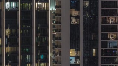 Şehrin hava zaman ayarlı yerleşim bölgesinde parlayan pencereleri olan uzun apartmanlar. Kulelerdeki ve gökdelenlerdeki odalarda akşam sarı ışığı