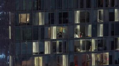 Kule binasının gece ön cephesinde ışık zamanlaması olan apartmanların bir sürü penceresi var. Her pencerede hayat var. Ofisin cam cephesinin ve yerleşim yerinin hava görüntüsü..