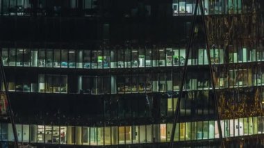 Ticari kule binasının gece ön cephesi. Bir sürü panoramik pencereli ve zaman ayarlı. Her pencerede hayat var. Bir ofis gökdeleninin cam cephesinin havadan görünüşü.