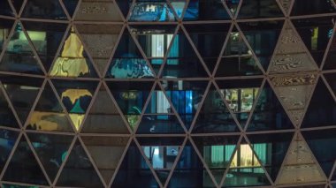 Kule binalarının aydınlık gece ön cephesi. Işıklı zaman ayarlı pencereleri var. Her pencerede hayat var. Yerleşim yeri gökdelenlerinin cam cephesinin havadan görünüşü.