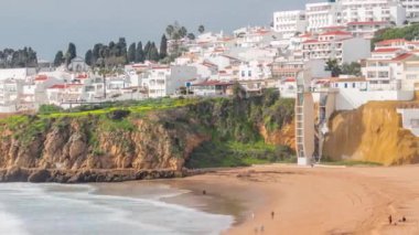 Geniş kumlu sahil ve Albufeira zamanındaki Atlantik Okyanusu. Uçurumun tepesindeki beyaz evler. Asansör perspektiften sahile doğru. Yukarıdan hava görüntüsü. Algarve, Portekiz