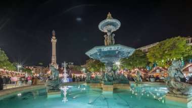 Portekiz, Lizbon 'un Baixa bölgesindeki Dom Pedro IV Meydanı' ndaki Rossio Noel Pazarı 'nda akşam süslemeleri ve yemek kabinleriyle aydınlatılmış çeşmeyi gösteren panorama..