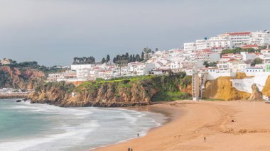 Geniş kumlu sahil ve Albufeira zamanındaki Atlantik Okyanusu. Uçurumun tepesindeki beyaz evler. Asansör perspektiften sahile doğru. Yukarıdan hava görüntüsü. Algarve, Portekiz